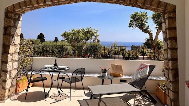 Une terrasse agrémentée d’une arche en pierre, une table avec des chaises, une petite table avec une plante et une chaise avec un magazine.