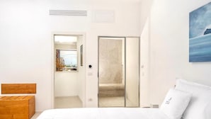 Une chambre à coucher avec un lit, une tête de lit en bois, une porte donnant sur une salle de bain et un tableau accroché au mur.
