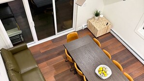 Un coin repas avec une table en bois, des chaises jaunes, un canapé vert et un ventilateur de plafond.