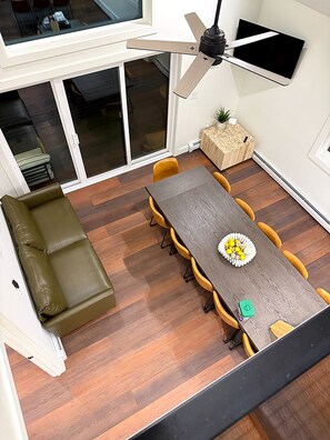 Ein Essbereich mit Holztisch, gelben Stühlen, einem grünen Sofa und einem Deckenventilator.