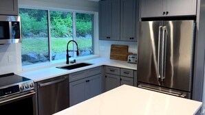 Une cuisine moderne dotée d’un grand îlot central, d’appareils électroménagers en acier inoxydable et d’une fenêtre donnant sur un paysage verdoyant.