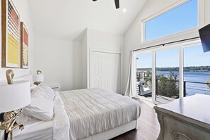 Une chambre avec une grande fenêtre, un lit, une table de chevet et une commode.