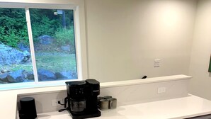Une cuisine équipée d’une machine à café, de placards et d’une fenêtre donnant sur un paysage verdoyant.