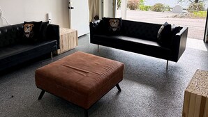 Un salon moderne avec deux canapés, un pouf marron et une grande fenêtre donnant sur un lac.
