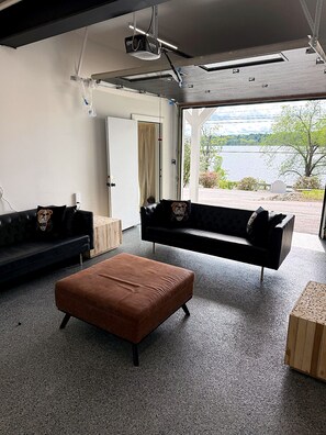 Ein modernes Wohnzimmer mit zwei Sofas, einem braunen Hocker und einem großen Fenster mit Seeblick.