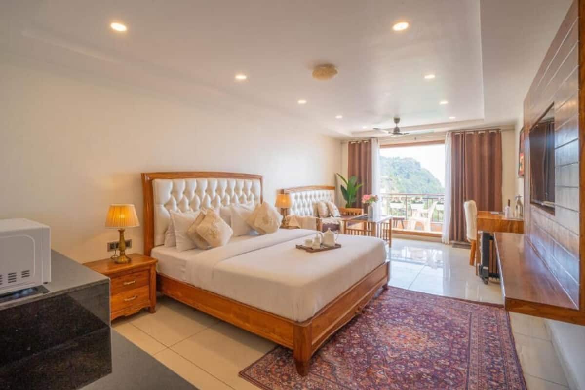 Habitación de hotel con cama, mesita de noche, lámpara y vistas al exterior.