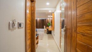 Un couloir avec des portes en bois, un mur blanc, un interrupteur et un thermostat.