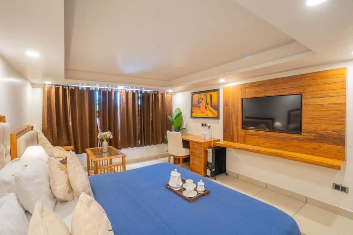 Una habitación de hotel con cama, escritorio, televisor y un amplio ventanal con cortinas.