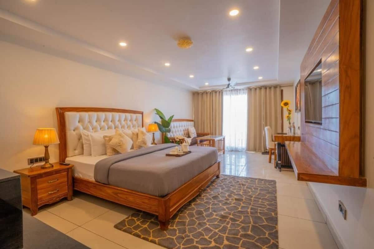 Un dormitorio con cama, mesitas de noche, escritorio, silla, televisión y una ventana grande.