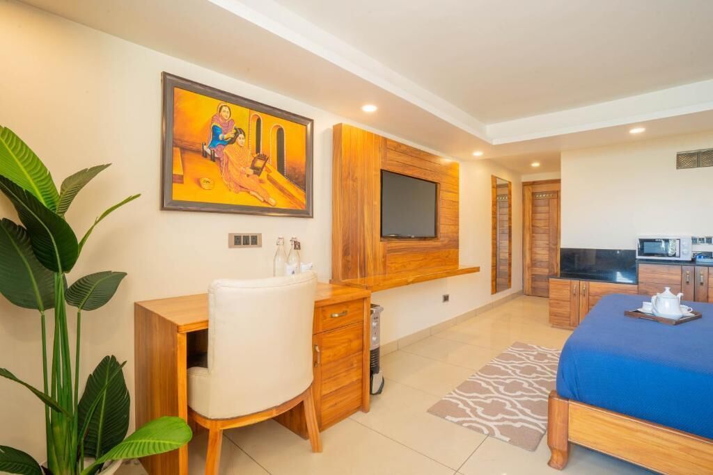 Une chambre d’hôtel équipée d’un lit, d’un bureau, d’un téléviseur fixé au mur, d’un four à micro-ondes et d’une grande plante.