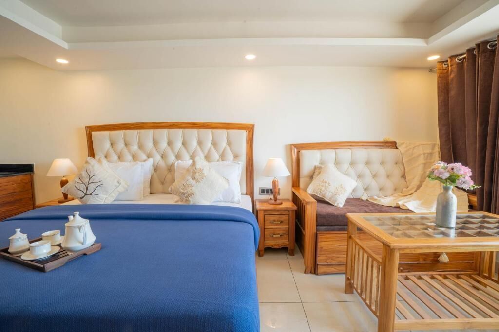A hotel room with two beds, a small table, and a bedside table with lamps.