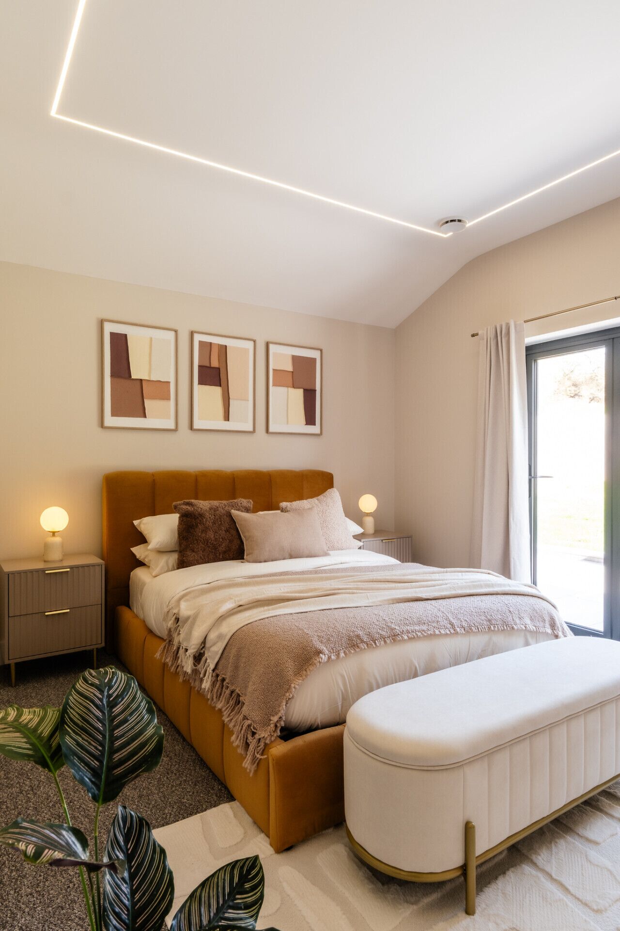 Een moderne slaapkamer met een bed, nachtkastjes, een bankje en kunst aan de muur.