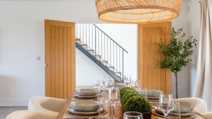 A dining area with a wooden table set for a meal, a woven pendant light, and a staircase in the background.