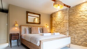 Een slaapkamer met een stenen muur, een houten bed, een nachtkastje en een spiegel.