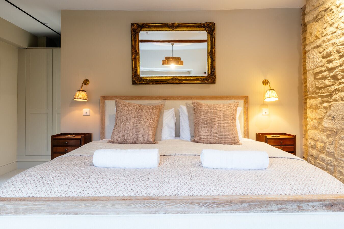 A neatly made bed with a patterned bedspread, two pillows, and two folded towels. There is a large mirror above the bed and two bedside lamps.