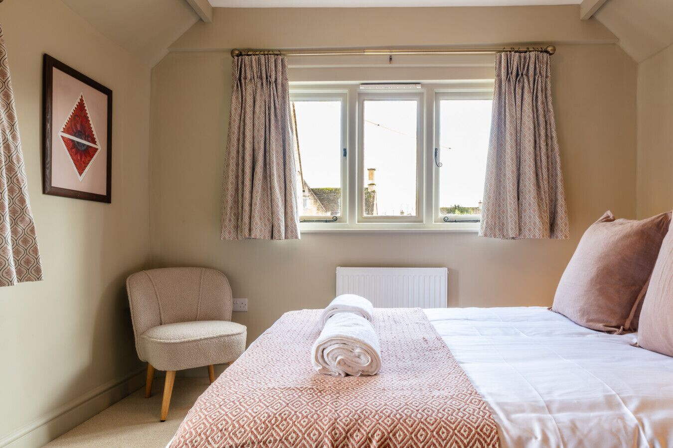 A bedroom with a bed, a chair, a radiator, and a window with curtains.