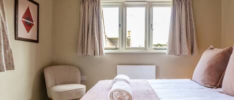 A bedroom with a bed, a chair, a radiator, and a window with curtains.