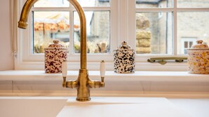A kitchen with a gold faucet, white cabinets, and three ceramic containers on the window sill. - The Haybarn | Banham Cottages (Bourton-on-the-Water)