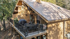 Una cabana de fusta amb un balcó, mobiliari d'exterior i una zona de barbacoa coberta.