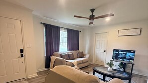 A living room with a sofa, a coffee table, a television, and a ceiling fan. - Cozy, Charming and very Convenient House (Spartanburg)