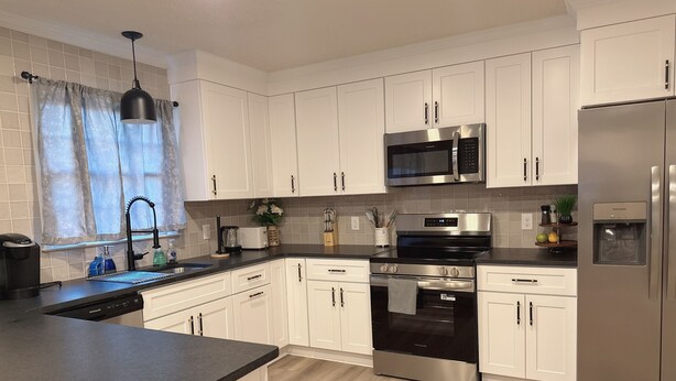 A modern kitchen with white cabinets, stainless steel appliances, and a black countertop. - Cozy, Charming and very Convenient House (Spartanburg)