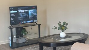 A living room with a TV, a console table, a round coffee table, and a plant. - Cozy, Charming and very Convenient House (Spartanburg)