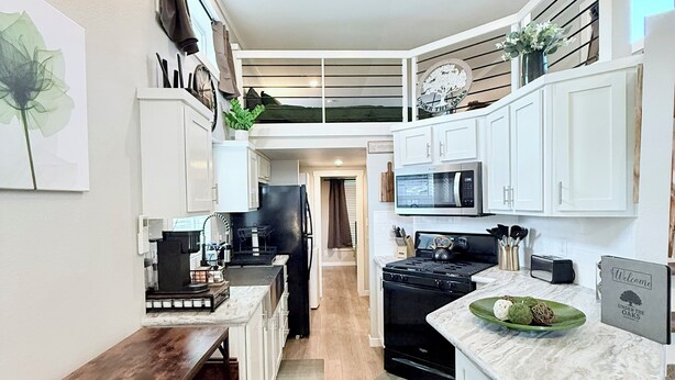 Una cocina moderna con armarios blancos, una estufa negra, un microondas y un comedor con un banco de madera.