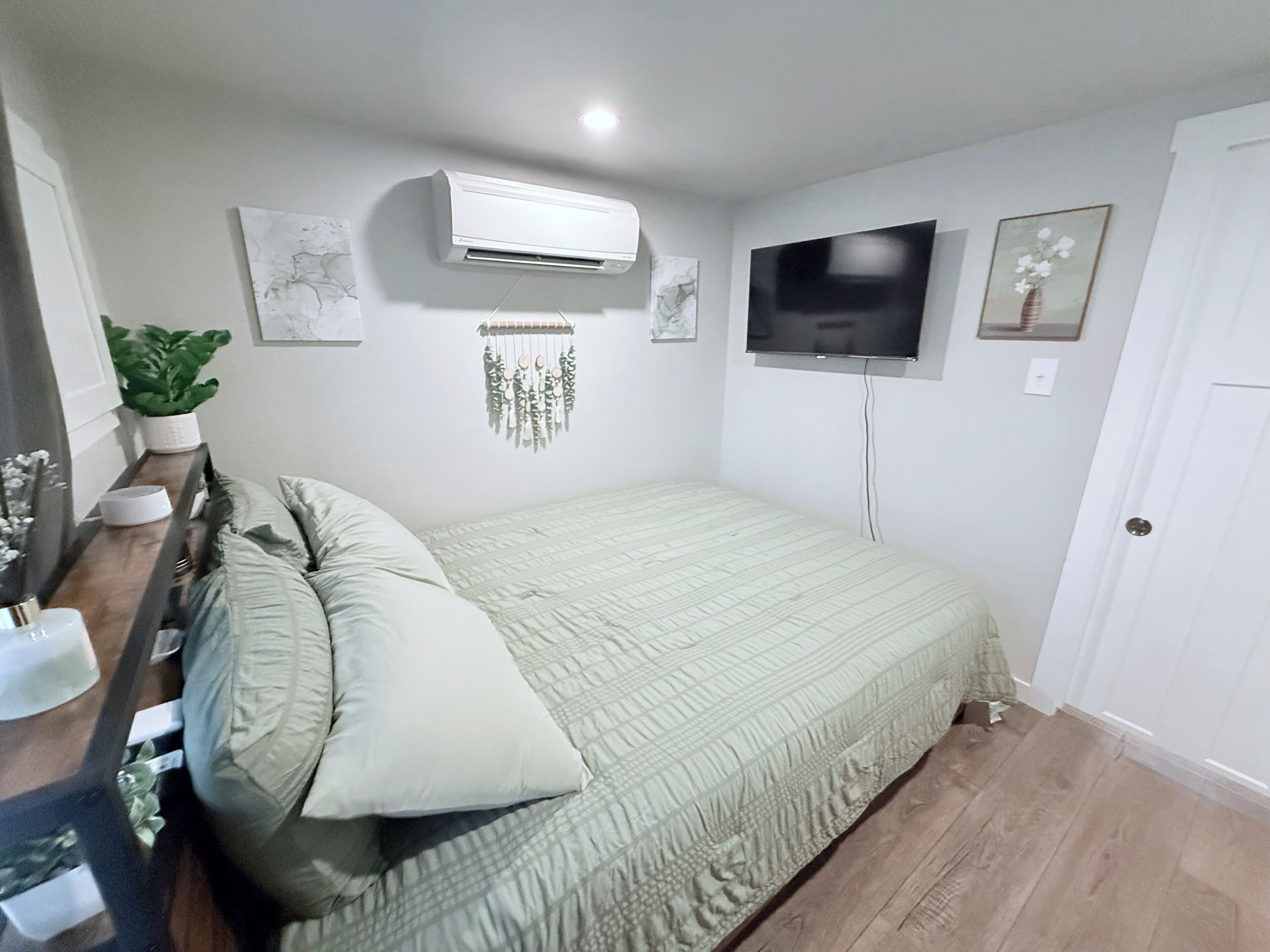A bedroom with a bed, a wall-mounted air conditioner, a flat-screen TV, and a door.