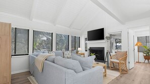 A modern living room with a grey sofa, a flat-screen TV, a fireplace, and large windows. - Fabulous 2 bed with a loft! Amenities included! Pets NOT allowed (Seabrook Island)