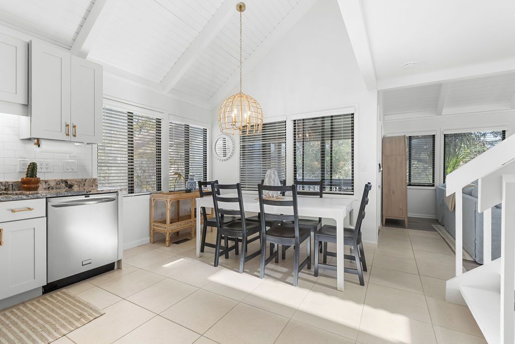 Una cocina moderna con armarios blancos, un comedor con mesa y sillas blancas, y una escalera que sube a otro nivel.