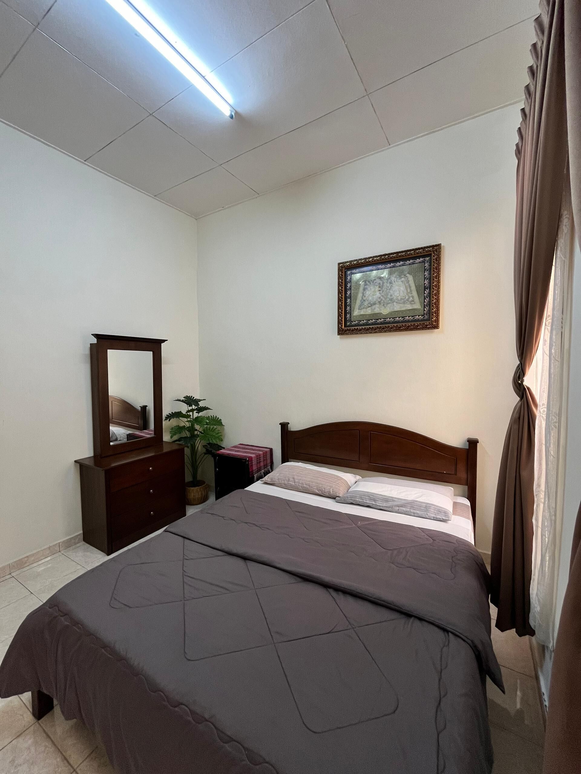 Un dormitorio ordenado con cama, cómoda, espejo y un cuadro en la pared.