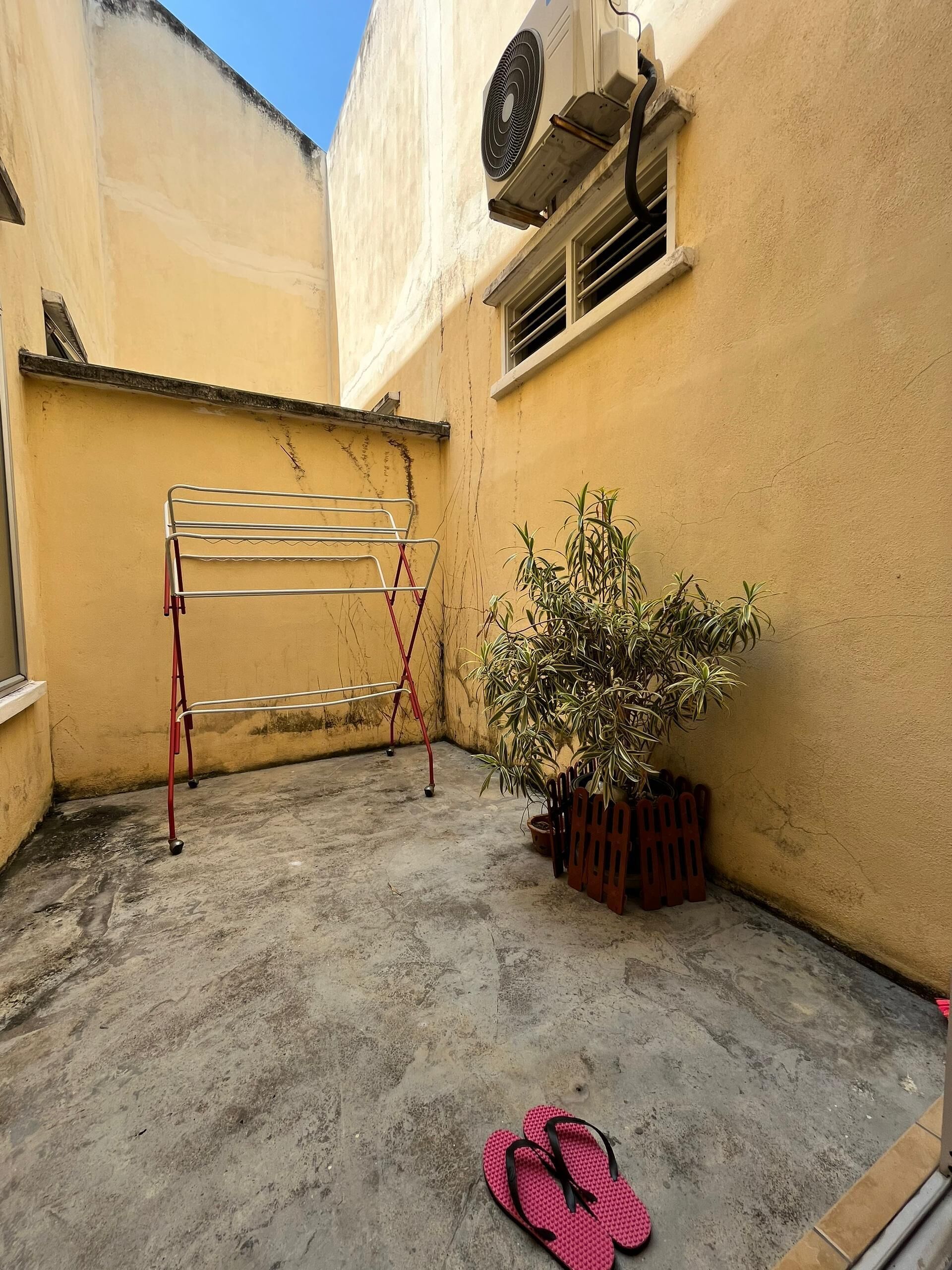 A small outdoor area with a metal drying rack, a potted plant, and a pair of flip-flops on the ground.