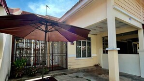 Un espace patio aménagé avec une table et des bancs, un grand parasol et une entrée fermée par un portail.