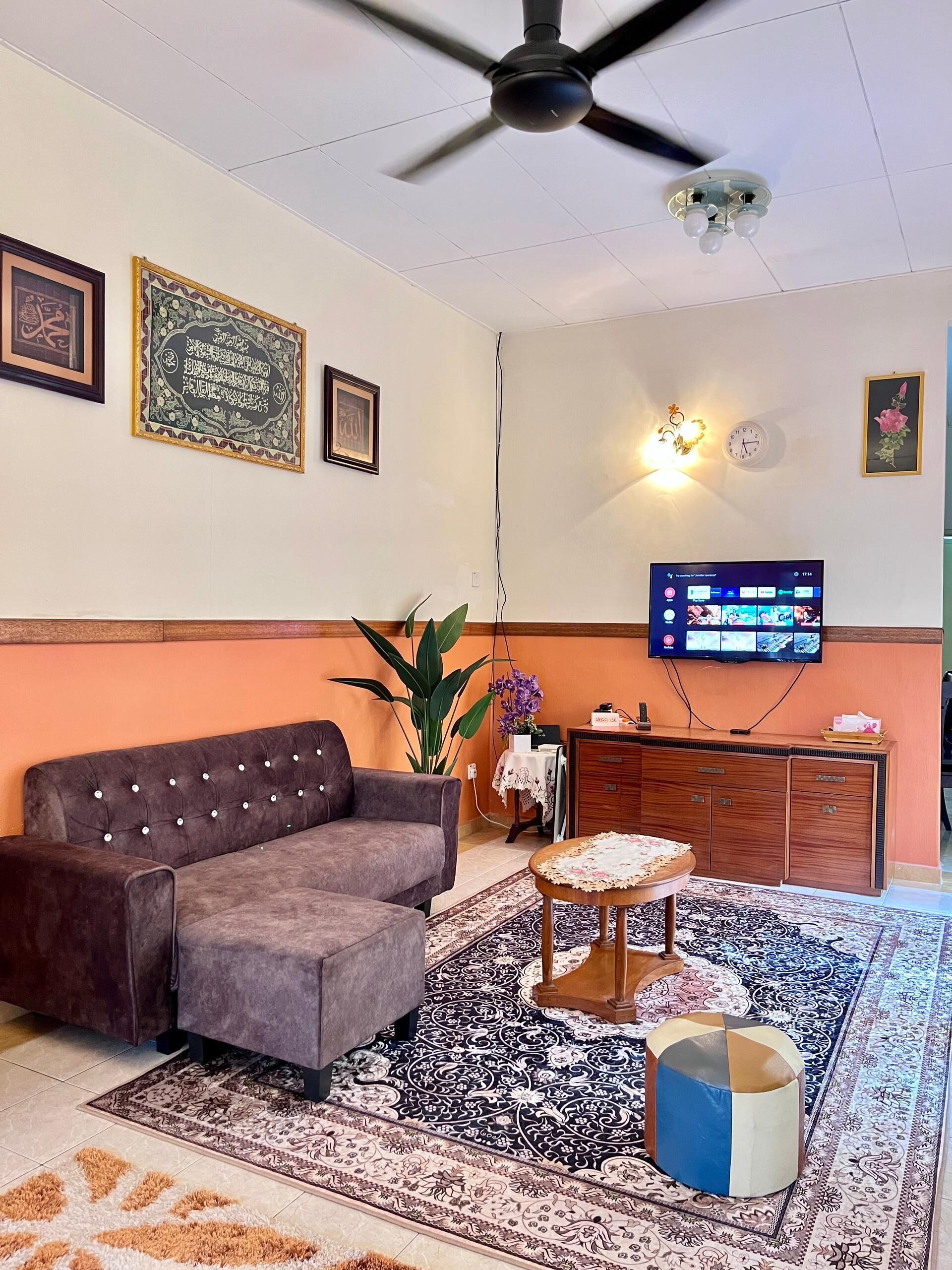 Un salon comprenant un canapé, un téléviseur, un ventilateur de plafond, une horloge et un élément décoratif mural.