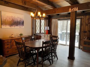 Un comedor con mesa y sillas de madera, un candelabro y un ventanal con cortinas.