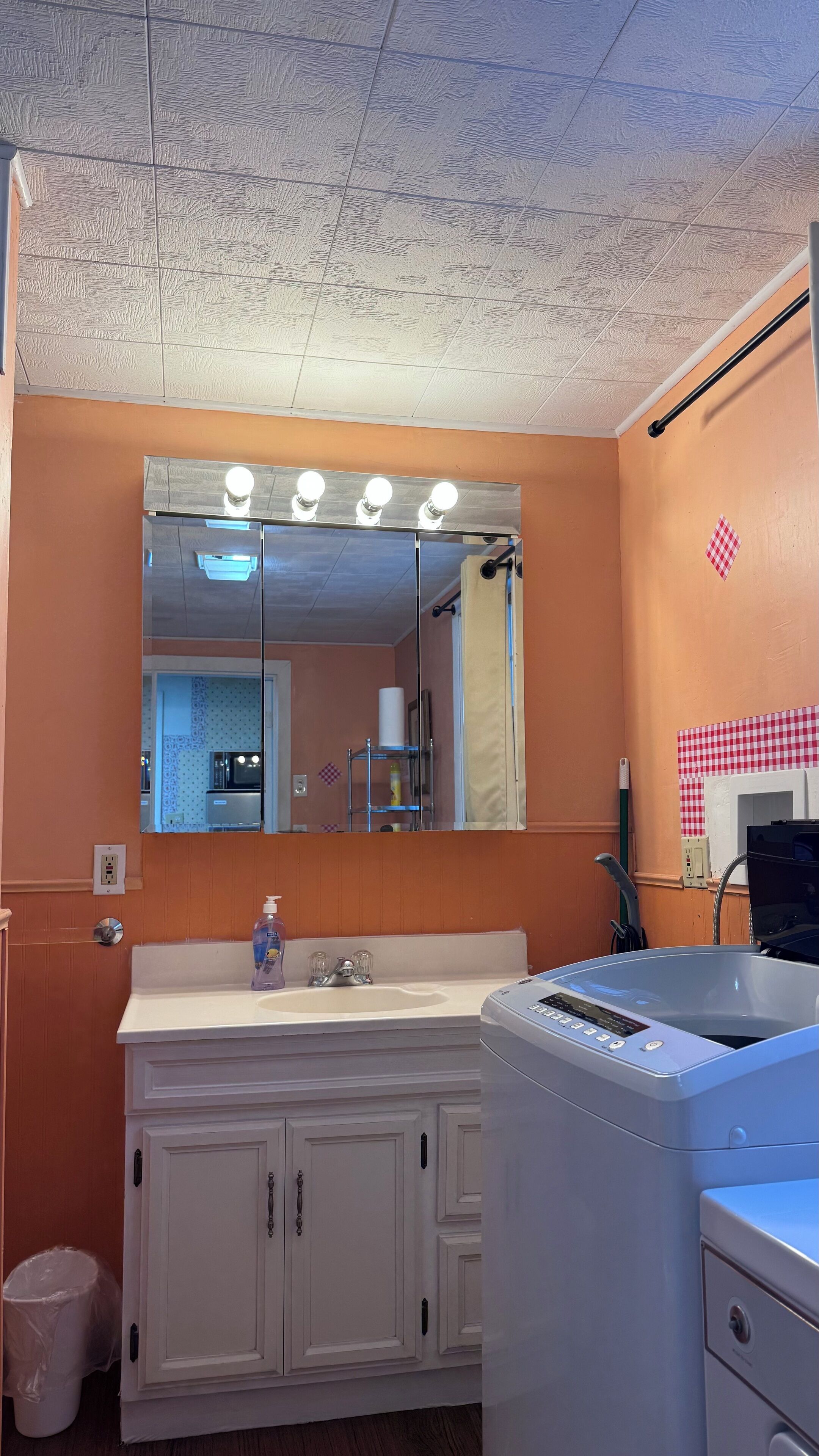 A bathroom with a white vanity, a large mirror with lights, a sink, a toilet, and a shower area.