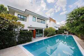 Una casa moderna de dos pisos con piscina, rodeada de vegetación.