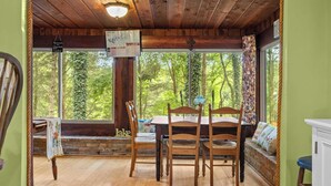 A wooden dining area with a table and chairs, a bench, and a view of trees through large windows.