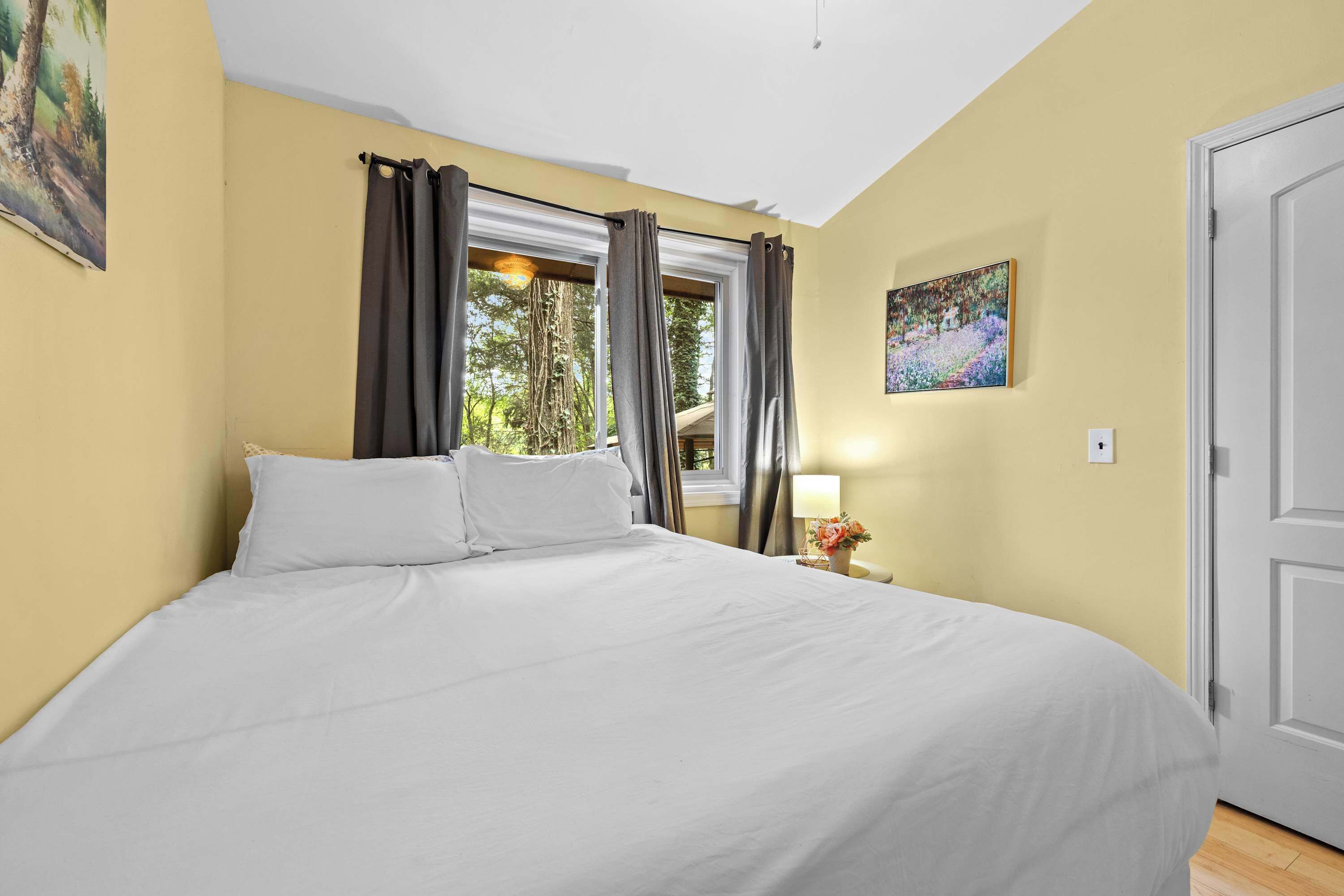 Une chambre à coucher avec un lit, des rideaux, une fenêtre, un tableau et une porte.