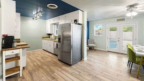 Cozinha moderna com geladeira de aço inoxidável, piso de madeira e área de jantar com mesa e cadeiras.