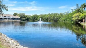 Un lac paisible avec une fontaine au centre, entouré d’une végétation luxuriante et d’un bâtiment situé sur la gauche.