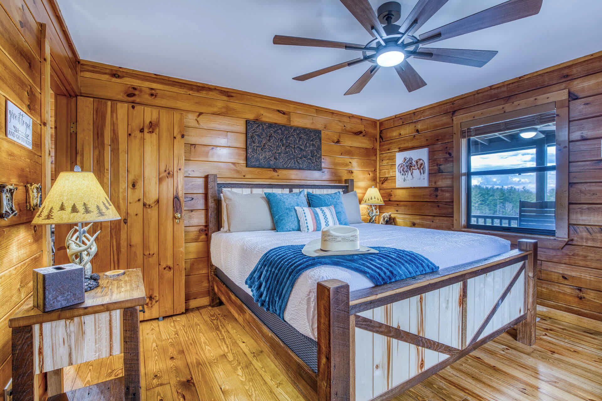 A wooden cabin bedroom with a bed, a ceiling fan, and a window with a view.