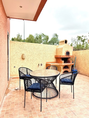 An outdoor patio with a round table and four chairs, a brick oven, and a tiled floor.