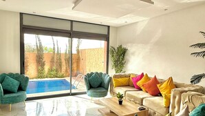 Ein modernes Wohnzimmer mit Sofa, Sesseln, einem Couchtisch und Blick auf einen Swimmingpool.