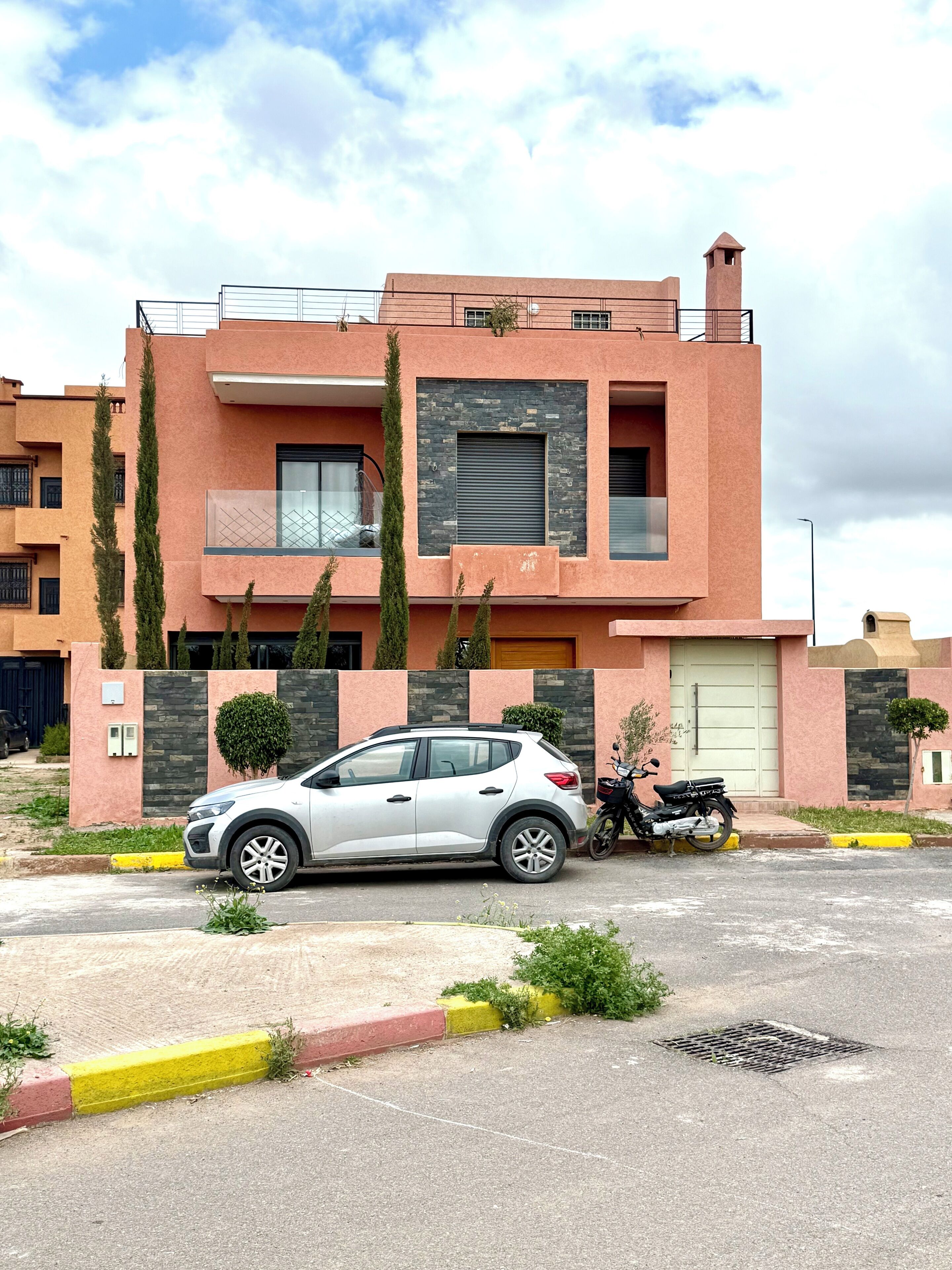 Un bâtiment moderne à deux étages, avec une voiture garée devant et une moto sur l’allée.