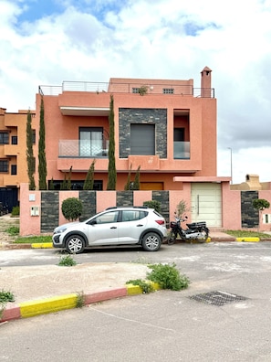 A modern two-story building with a car parked in front and a motorcycle on the driveway.