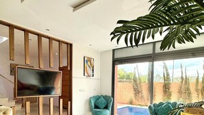 Ein modernes Wohnzimmer mit Flachbildfernseher, bequemen Sofas, einem großen Fenster mit Blick auf einen Pool und einer Zimmerpflanze.