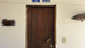 En dörr av trä med ett mässingshandtag, två blå skyltar som visar var toaletterna finns, placerade ovanför dörren, och en fiskdekoration till höger.
