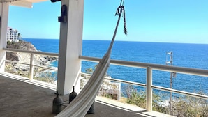 En hängmatta under ett vitt tak med utsikt över havet och den steniga kustlinjen.