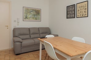 A room with a grey sofa, a wooden table, white chairs, and framed botanical prints on the wall.